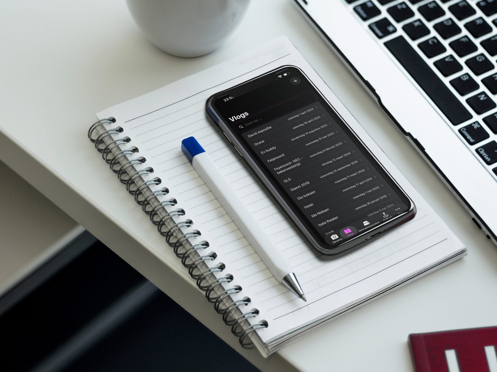 FilmSticks app on iPhone on a notebook on an office desk, showing the vlogs filter view